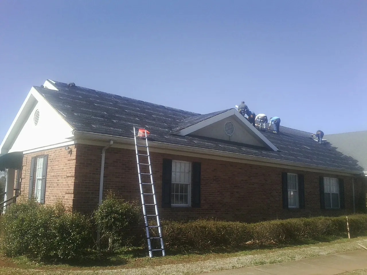 Crew tearing shingles off a brick ranch roof with a ladder set — Metal Roof Repair work by our crew in Woodbury