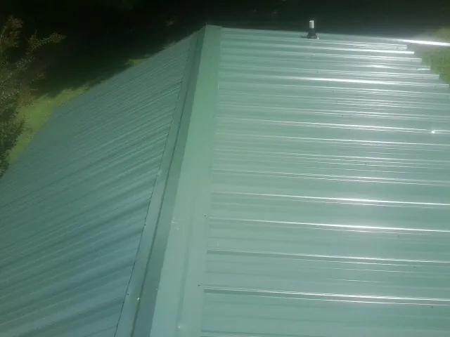 New green metal panels meeting at the ridge of a roof — Flat Roof Repair work by our crew in Woodbury