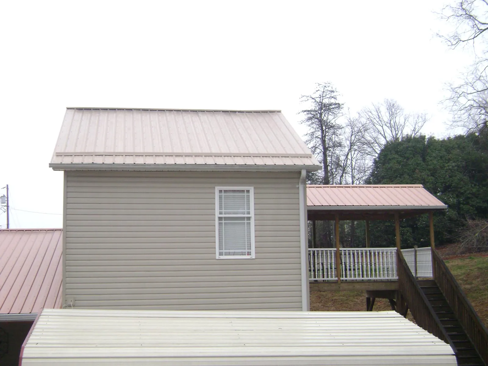Tan metal roofs on a two story addition and attached porch, from a Roof Replacement job in Woodbury